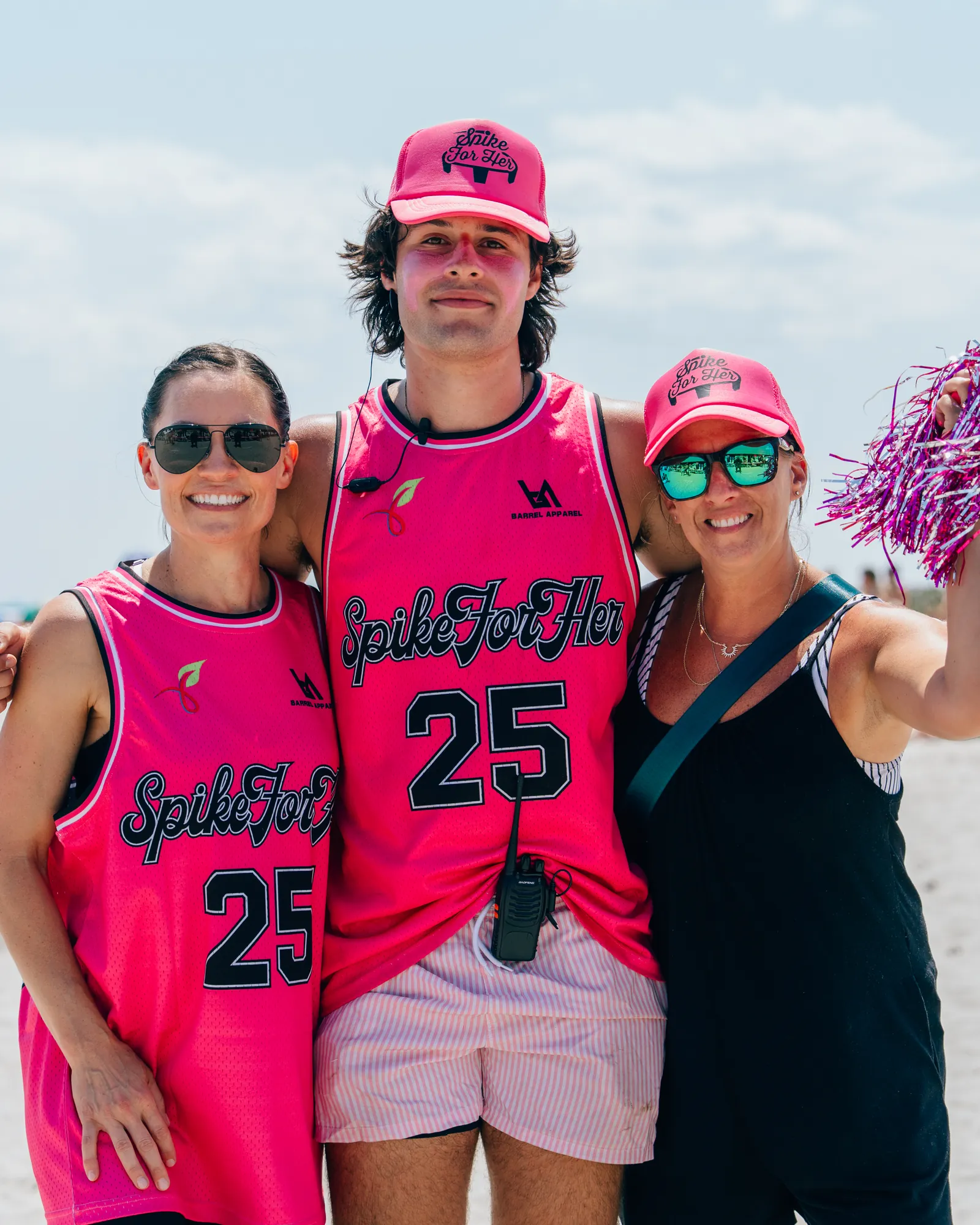 Zeke in a pink Spike For Her jersey and cap with his mom and family at the event tent, holding pink pom-poms