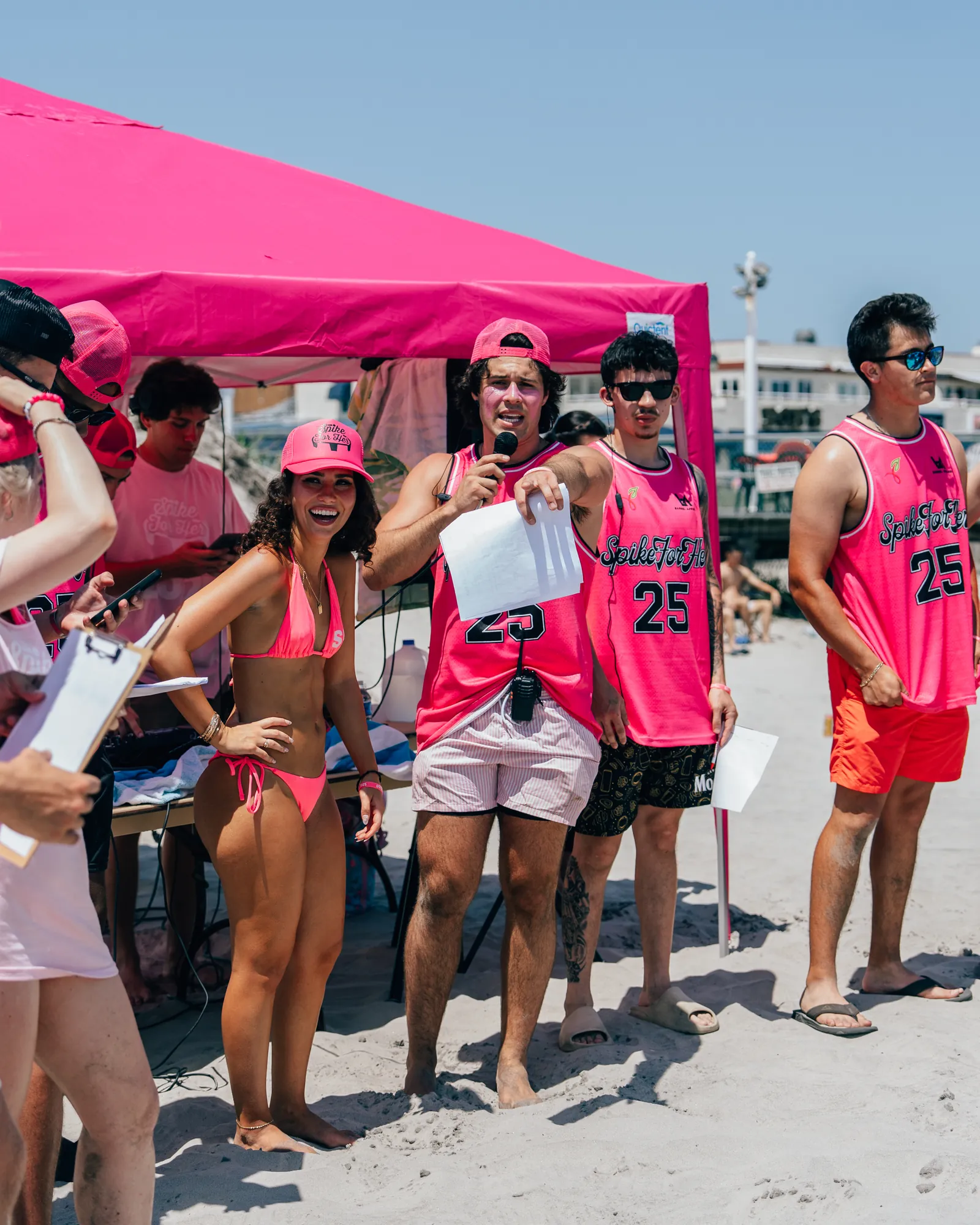 Erin Pellegrin of Unite for HER in a pink Spike For Her jersey speaking on the microphone, surrounded by players