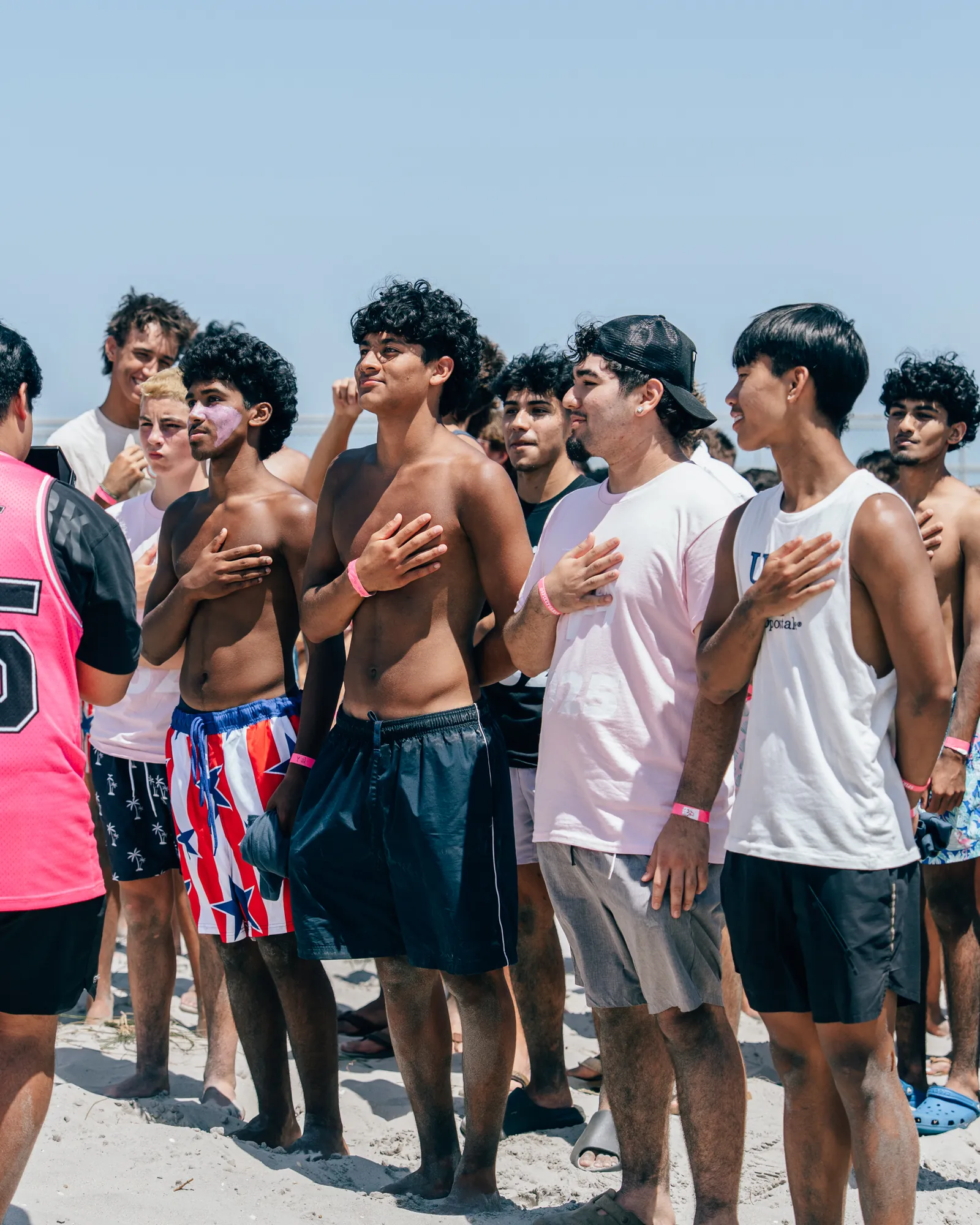 Players standing in a line on the sand with hands over their hearts during the national anthem